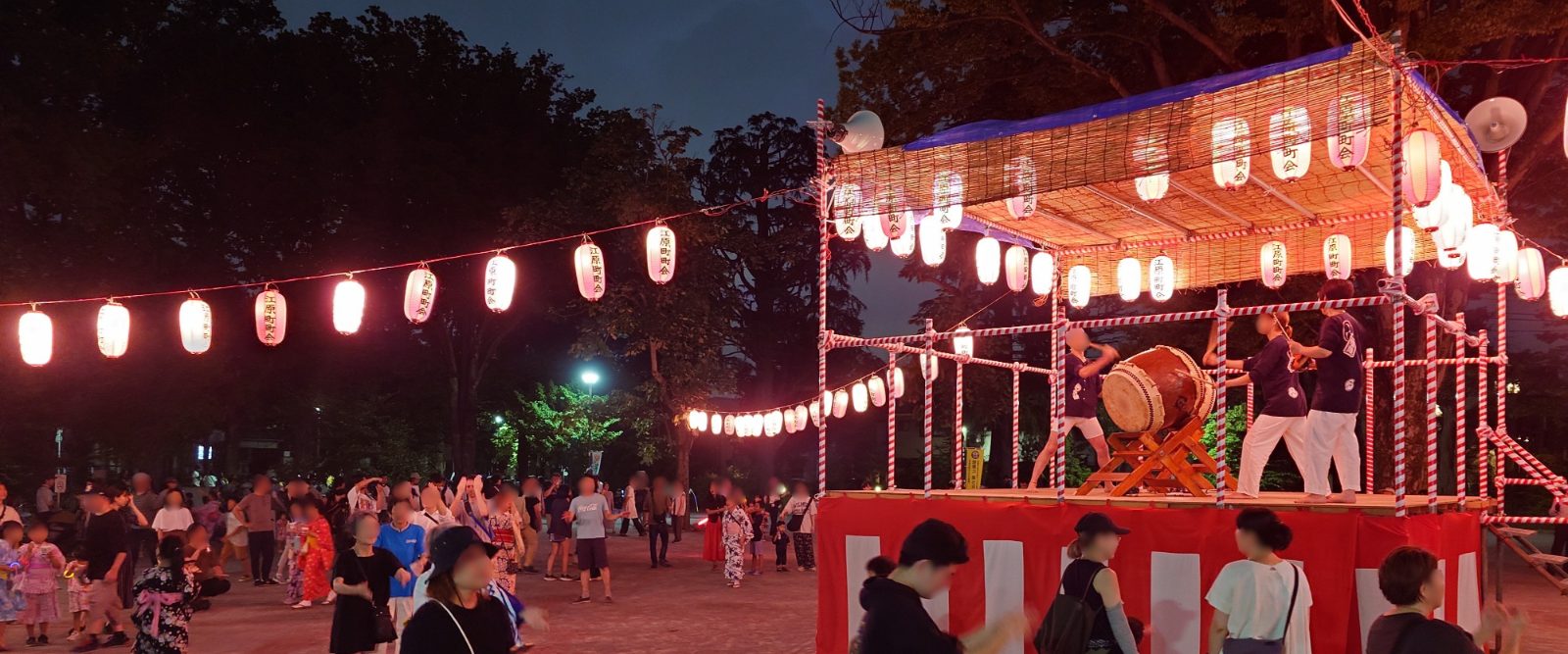 納涼盆踊り大会の櫓で太鼓を打つ演者と、「江原町町会」と書かれた提灯の連なり